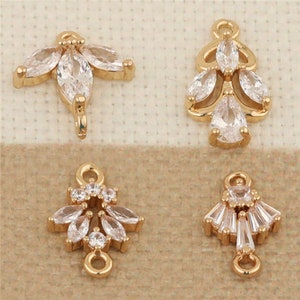 May include: Four gold-tone metal charms with clear crystal embellishments. Each charm features a different design with a loop at the top for attaching to jewelry.
