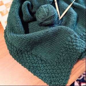 Könnte beinhalten: Ein dunkelgrüner Strick Schal mit einer Wollknäuel und Stricknadeln.