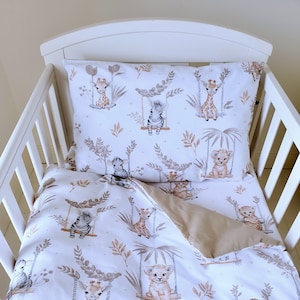 May include: White cot bedding set with a safari animal print. The bedding features giraffes, zebras, and lions on a white background with brown and beige accents. The set includes a fitted sheet, a flat sheet, and a pillowcase.