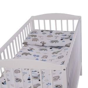 Peut inclure: Un lit bébé blanc avec un drap-housse imprimé d'animaux de la savane blanc et bleu et une taie d'oreiller assortie. Le drap-housse présente une variété d'animaux, dont des lions, des éléphants, des girafes et des zèbres. La taie d'oreiller a un design similaire, mais avec une disposition légèrement différente des animaux.