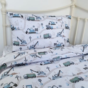 Peut inclure: Literie blanche avec un motif de véhicules de chantier bleus et verts. La literie présente une variété de véhicules de chantier, notamment des excavatrices, des camions à benne basculante et des bulldozers. Le motif est répété sur la taie d'oreiller et la housse de couette.