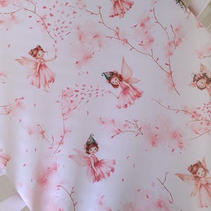 May include: A white cot sheet featuring a repeating pattern of fairies, pink blossoms, and branches. The fairies are in pink dresses with wings, some wearing flower crowns or hats. The design has a watercolour effect.