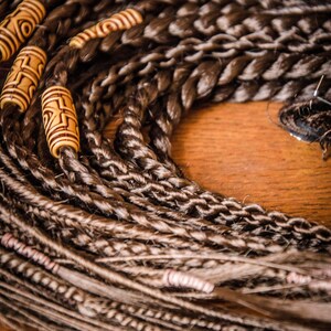 Puede incluir: Primer plano de un paquete de rastas sintéticas marrones y rubias con cuentas de madera. Las rastas están dispuestas en círculo, con las cuentas en la parte superior del círculo.