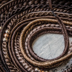 Könnte beinhalten: Nahaufnahme einer Sammlung von braunen und blonden synthetischen Haarverlängerungen mit Perlen. Die Verlängerungen sind geflochten und in einem Kreis angeordnet.