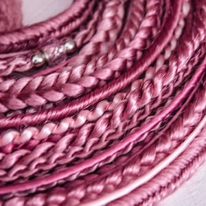 May include: Close-up of a bundle of pink and white braided hair extensions. The hair is arranged in a circle and has a subtle sheen.