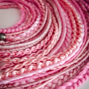 Puede incluir: Primer plano de un manojo de hilo rosa y blanco, con diferentes texturas y trenzas. El hilo está dispuesto en forma circular, creando un patrón visualmente atractivo.