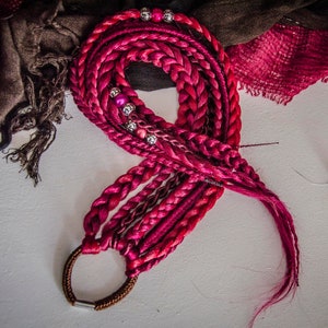May include: A set of pink and black synthetic hair extensions with beads and a brown elastic band.