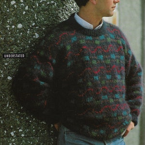 Könnte beinhalten: Ein dunkelblauer Pullover mit einem bunten geometrischen Muster. Der Pullover hat einen Rundhalsausschnitt und lange Ärmel.