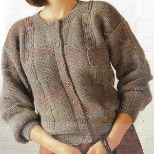 Può includere: Un cardigan di maglia marrone, beige e rosa con un motivo a treccia e chiusura con bottoni.