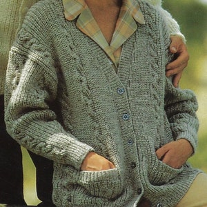 Könnte beinhalten: Ein grauer Strickcardigan mit Zopfmuster, V-Ausschnitt und Knopfleiste. Der Cardigan hat zwei Taschen und ist aus einem weichen, warmen Material gefertigt.