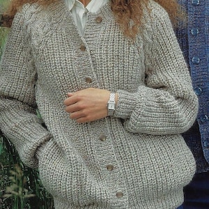 Op de afbeelding: Een grijze gebreide cardigan met een knoopsluiting en zakken. De cardigan heeft een geribbelde textuur en is gemaakt van een zacht, warm materiaal.