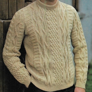 May include: A beige knitted jumper with a cable knit pattern. The jumper has a crew neck and long sleeves.