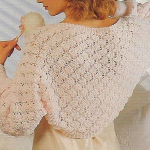 Könnte beinhalten: Eine weiße Häkeljacke mit einem zarten Lochmuster. Die Jacke hat lange Ärmel und eine verkürzte Länge.