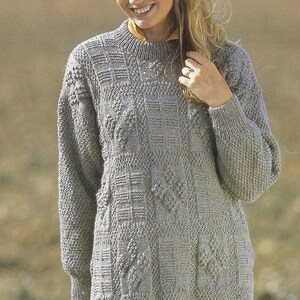 K&ouml;nnte beinhalten: Ein grauer Strickpullover mit einem strukturierten Muster. Der Pullover hat einen runden Ausschnitt und lange &Auml;rmel.