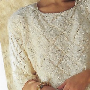 May include: A white knitted jumper with a delicate lace pattern. The jumper has a round neckline and three-quarter sleeves.