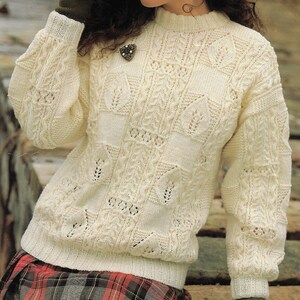 K&ouml;nnte beinhalten: Ein wei&szlig;er Strickpullover mit einem Zopfmuster und einer zarten Spitzenborte. Der Pullover hat einen runden Ausschnitt und lange &Auml;rmel.