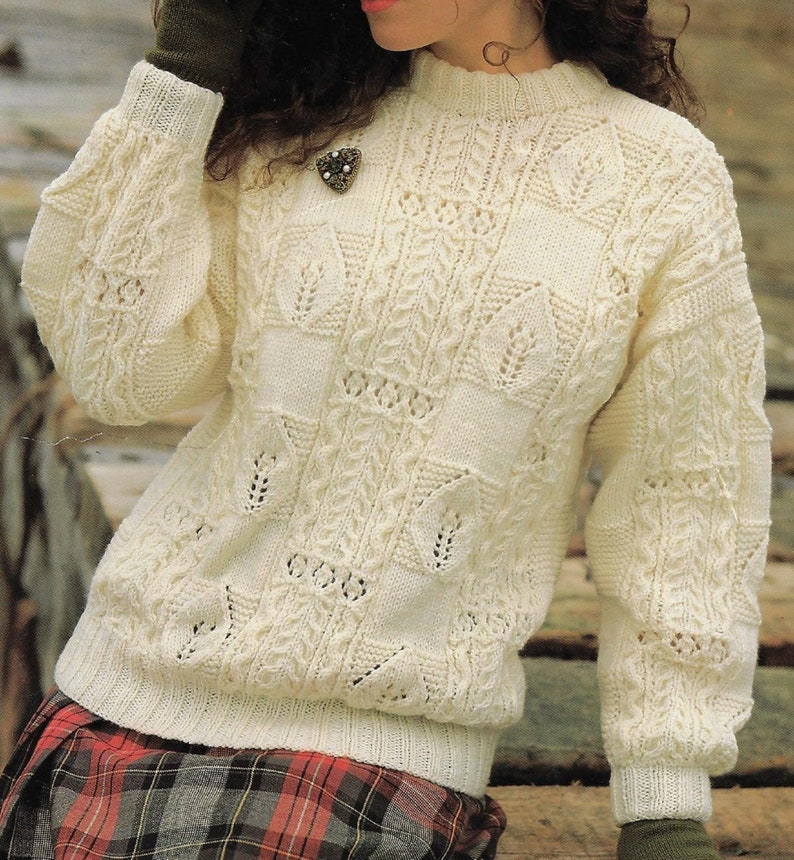 K&ouml;nnte beinhalten: Ein wei&szlig;er Strickpullover mit einem Zopfmuster und einer zarten Spitzenborte. Der Pullover hat einen runden Ausschnitt und lange &Auml;rmel.