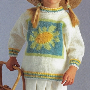 May include: White knitted sweater with a green, yellow, and blue flower design. The sweater has yellow and blue stripes on the cuffs and hem.
