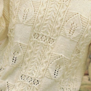 K&ouml;nnte beinhalten: Nahaufnahme eines wei&szlig;en Strickpullovers mit einem zarten Spitzenmuster. Der Pullover hat ein strukturiertes, durchbrochenes Design mit einem sich wiederholenden Blattmotiv.
