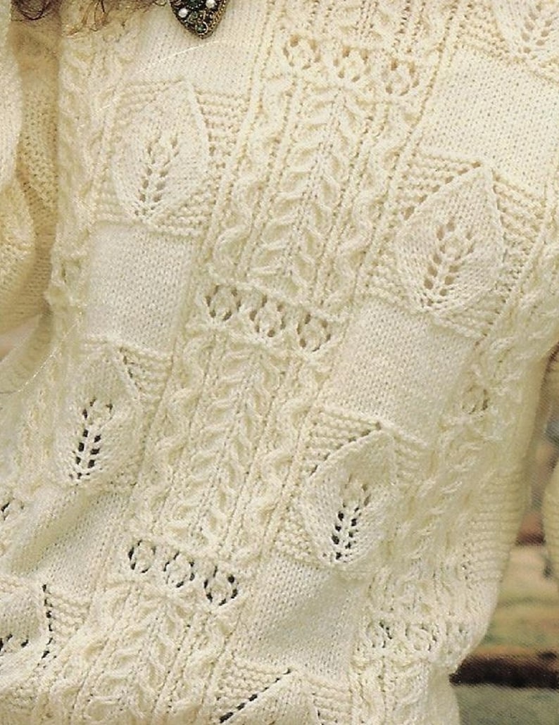 K&ouml;nnte beinhalten: Nahaufnahme eines wei&szlig;en Strickpullovers mit einem zarten Spitzenmuster. Der Pullover hat ein strukturiertes, durchbrochenes Design mit einem sich wiederholenden Blattmotiv.