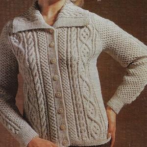 Op de afbeelding: Een crèmekleurige gebreide cardigan met een kabelbreipatroon en een grote kraag. De cardigan heeft een knoopsluiting en lange mouwen.