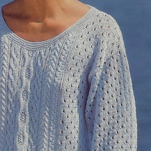 Puede incluir: Un suéter de punto azul claro con un patrón de trenza en la parte delantera y un patrón de encaje en las mangas.