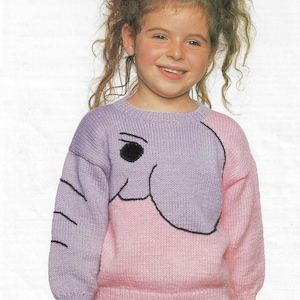 May include: A young girl wearing a pink and purple sweater with an embroidered elephant design. The sweater has long sleeves and a crew neck.