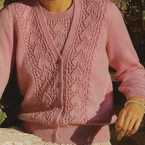 May include: A pink knitted cardigan with a button-up front and a delicate diamond-shaped lace pattern. The cardigan has long sleeves and a V-neck.