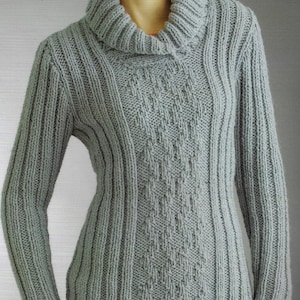 以下が含まれることがあります： グレーのケーブル編みのニットセーターで、タートルネックです。