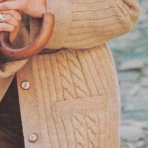 May include: A beige knitted cardigan with a cable knit pattern and two button closures. The cardigan has a patch pocket on the front.