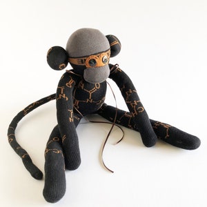 May include: A black and brown sock monkey with a gray hat and brown eyes. The monkey is sitting on a white surface.