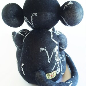Puede incluir: Mono de calcet&iacute;n negro y blanco con un dise&ntilde;o de esqueleto. El mono est&aacute; sentado con la cola enroscada alrededor de su cuerpo. El mono tiene una etiqueta que dice "Exclusively Handmade by The Sock Monkey Shop".