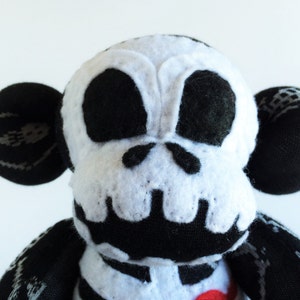 Puede incluir: Un mono de peluche blanco y negro con un dise&ntilde;o de calavera en la cara. El mono tiene grandes ojos negros y una nariz negra. El juguete est&aacute; hecho de tela suave y mullida.
