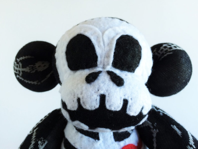 Puede incluir: Un mono de peluche blanco y negro con un dise&ntilde;o de calavera en la cara. El mono tiene grandes ojos negros y una nariz negra. El juguete est&aacute; hecho de tela suave y mullida.