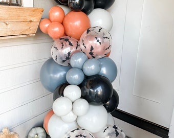 May include: A Halloween balloon arch with a variety of colors and patterns, including black, white, gray, orange, and clear balloons with bat silhouettes.