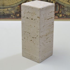 May include: A rectangular, light beige stone pillar with a textured surface. The pillar is a neutral color and stands upright. The background features a vintage world map.
