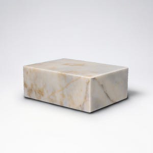 May include: A rectangular block of marble with a cream and tan color scheme. The stone has natural veining patterns, and the block is set against a white background. The object is a solid, geometric shape.