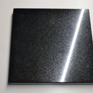 May include: A black square tile with a shiny, speckled surface. A bright white light reflects off the surface, creating a diagonal line.