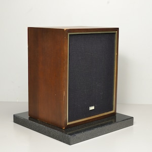 May include: A wooden speaker with a black fabric speaker grille and a gold trim. The speaker is sitting on a black granite base.