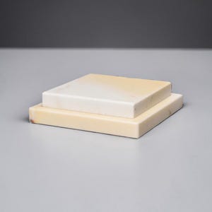 May include: Two rectangular, stacked blocks. The bottom block is a light beige color, while the top block is white with a slight yellow gradient. The blocks are smooth and appear to be made of stone or a similar material.