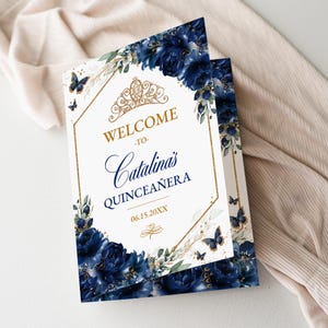 May include: A navy blue and gold quinceañera welcome sign with floral and butterfly accents. The sign features the text "Welcome to Catalina's Quinceañera" in elegant script, with the date 06.15.20XX.