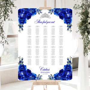 May include: A white seating chart with blue floral accents and the text "Please find your seat." The chart is decorated with blue flowers and a silver tiara. The event is for Catalina's Quinceañera.