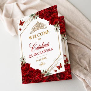 May include: A folded invitation with a white background, featuring red roses, butterflies, and gold accents. The text reads "Welcome to Catalina's Quinceañera" with the date 06.15.20XX. The design includes a gold crown and floral elements.