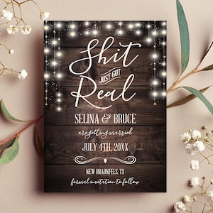 Peut inclure: Invitation de mariage rustique avec un fond en bois et des guirlandes lumineuses. Le texte indique "Shit Just Got Real" avec les noms du couple et la date du mariage.