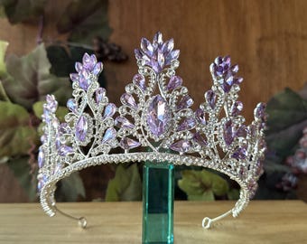 May include: A silver tiara with a purple and iridescent crystal design. The tiara has a pointed crown and a delicate, curved base.