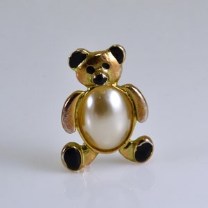 Peut inclure: Une broche en forme d'ours en or avec des accents noirs et une perle blanche au centre.