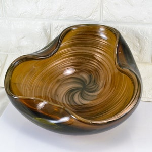 May include: A brown glass bowl with a swirl design. The bowl has a wavy edge and a shiny finish.