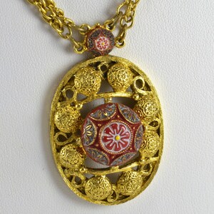 May include: A gold tone necklace with a large oval pendant. The pendant features a red, white, and blue enamel design with a floral motif. The necklace is made of a chain link style.