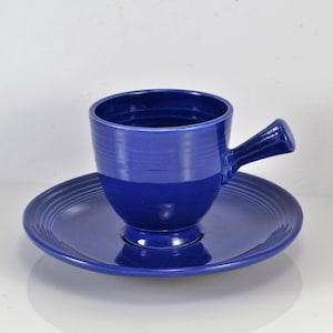 May include: A blue ceramic teacup and saucer set. The cup has a unique handle and a rounded shape. The saucer has a ridged design.