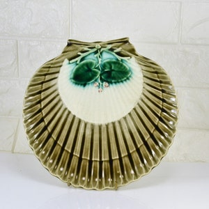 May include: A green and white ceramic shell-shaped dish with a raised floral design. The dish is perfect for serving snacks or appetizers.